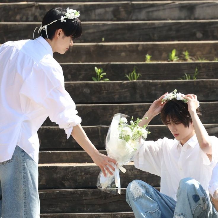 two people sitting on the ground with flowers in their hair and one person holding his hand