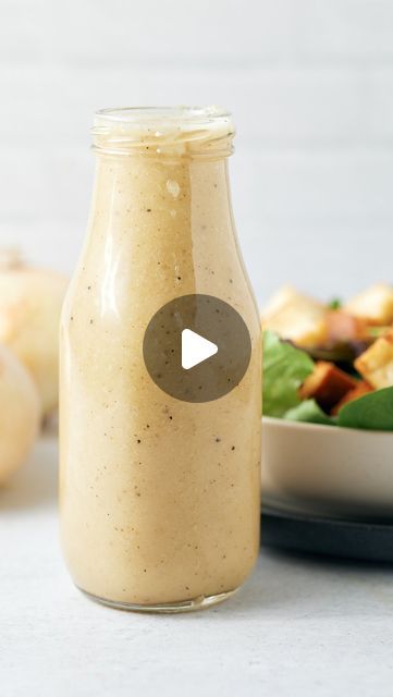 a glass jar filled with dressing next to a bowl of vegetables