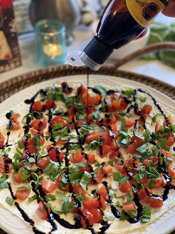 someone is spreading sauce on a pizza with tomatoes and lettuce as toppings