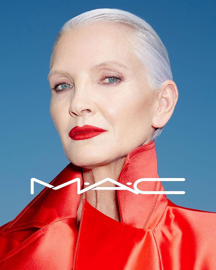 an older woman with white hair and bright red lipstick, wearing a red jacket that has the word mac on it