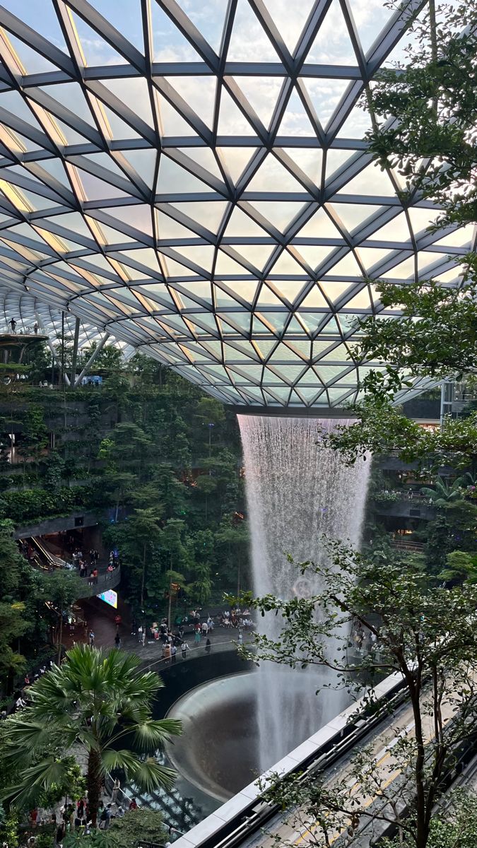 an indoor waterfall in the middle of a tropical area with trees and people walking around