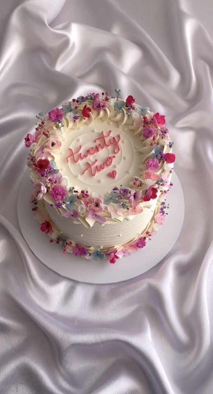 a white cake with pink and blue frosting on top of a white table cloth