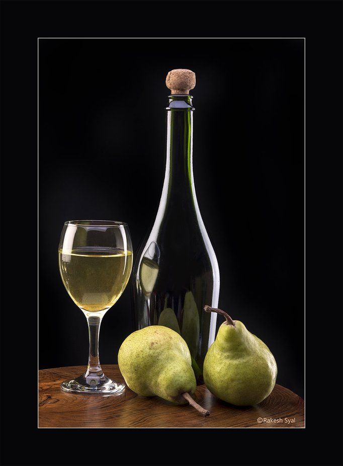 two pears and a bottle of wine on a table with a glass next to it