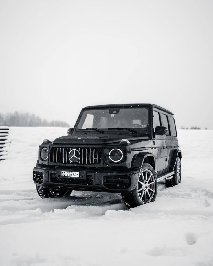 a black and white photo of a mercedes g - class parked in the middle of snow