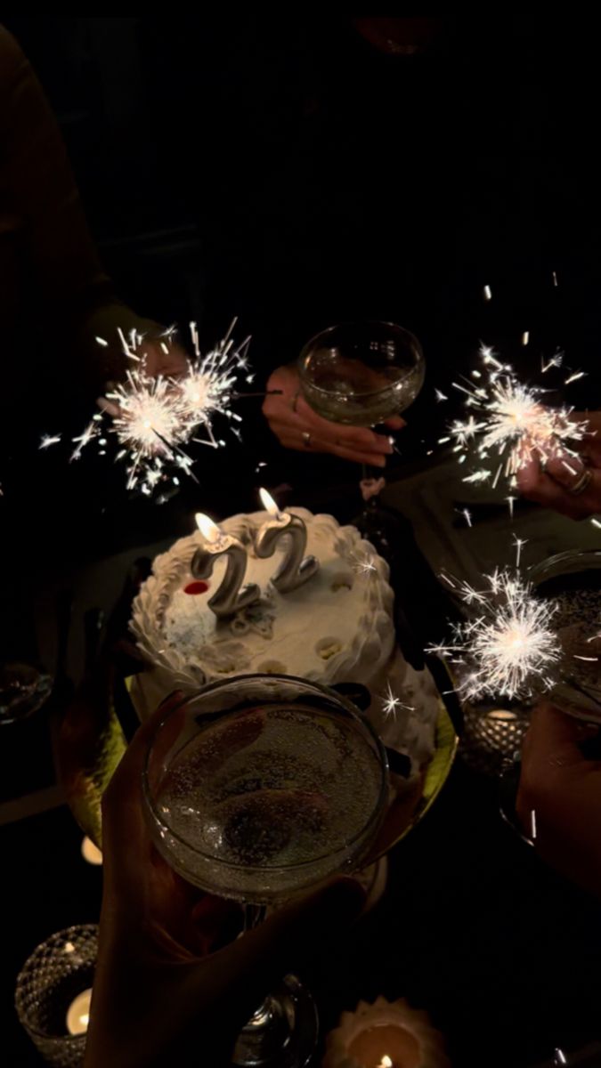 people are holding sparklers over a cake with candles on it and one person is holding a wine glass in front of the cake