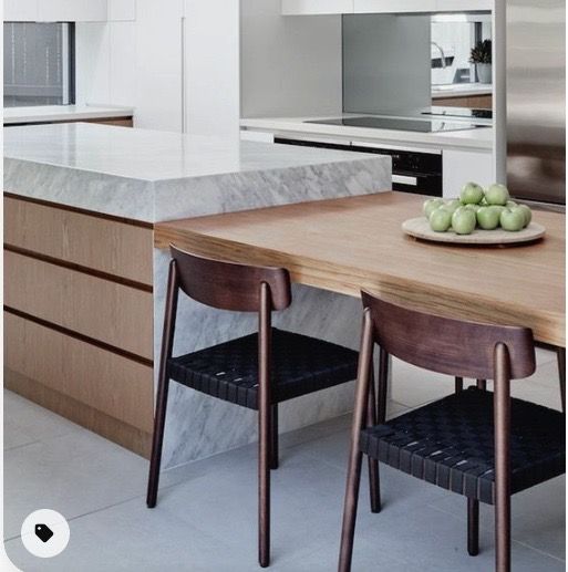 a kitchen with marble counter tops and wooden chairs in front of an island that has fruit on it