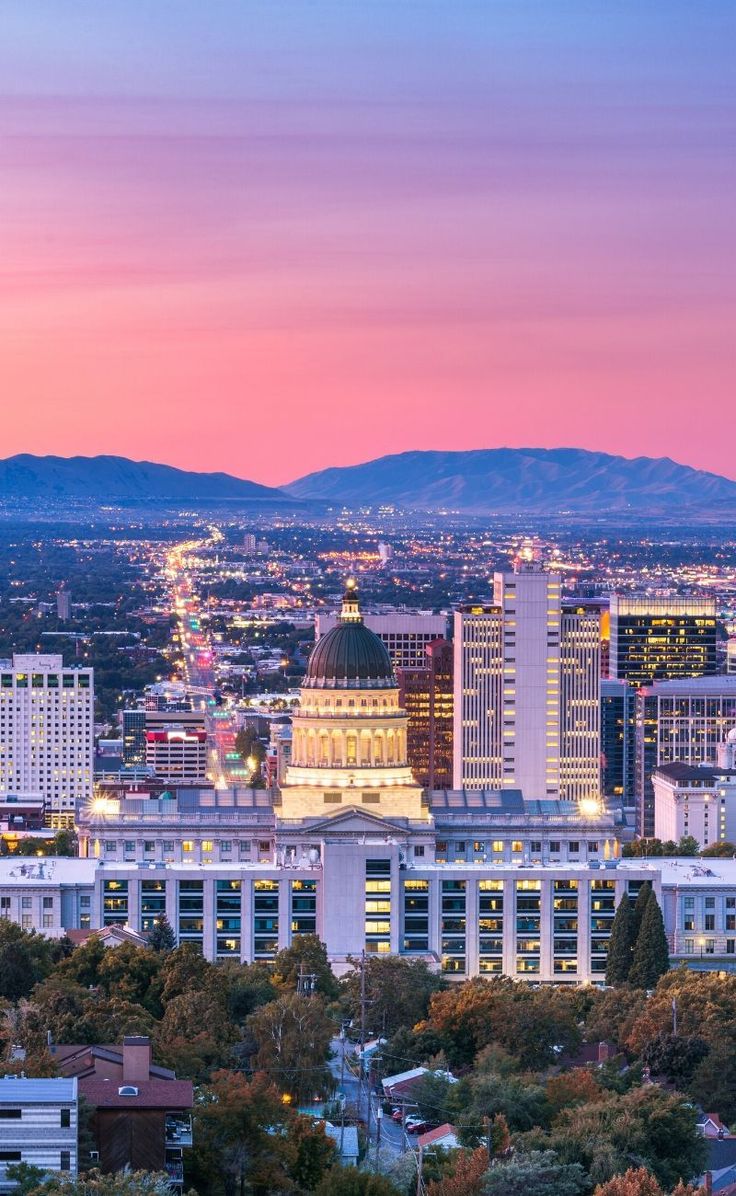 the city skyline is lit up at night with mountains in the backgrouund