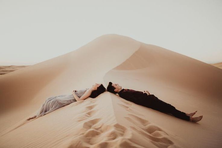 two people laying down in the middle of an empty desert with sand dunes behind them