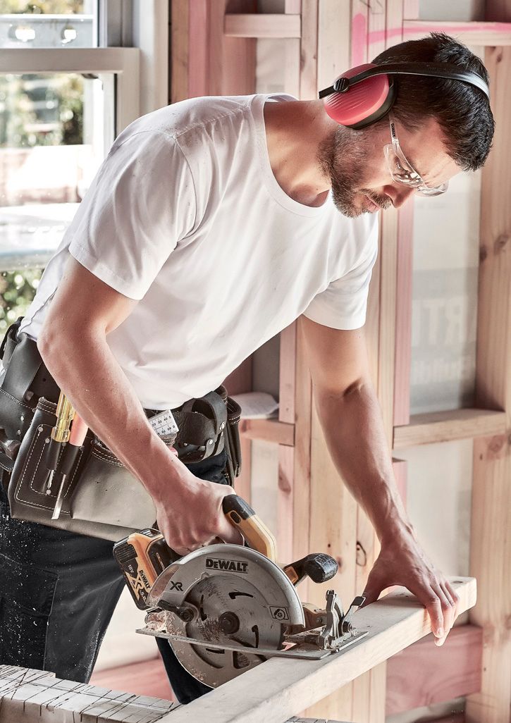 a man in white shirt using a circular saw to cut wood with a mitt