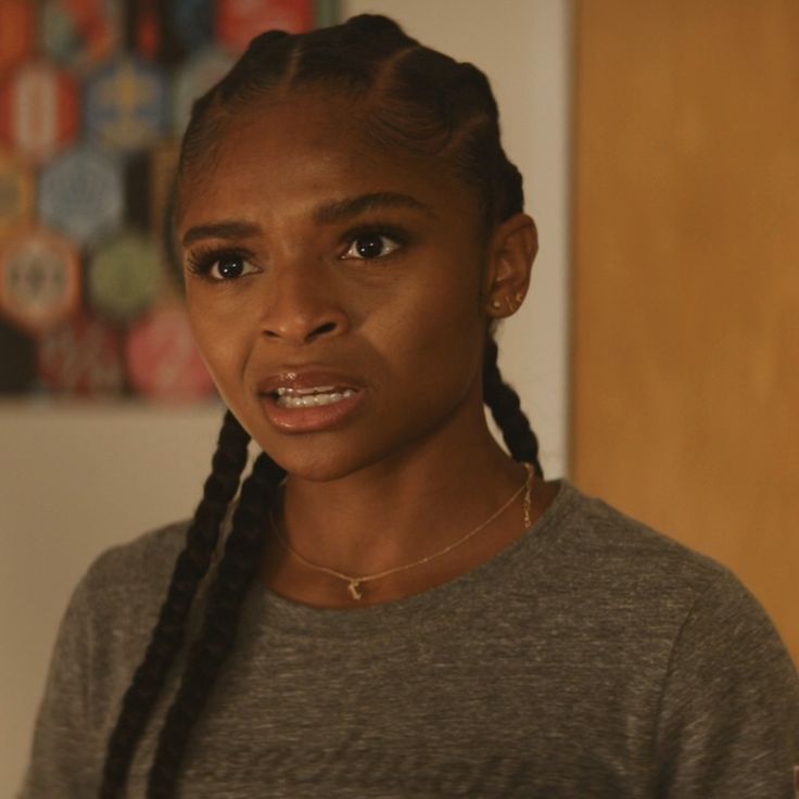 a woman with braids on her hair looking at the camera while wearing a gray shirt