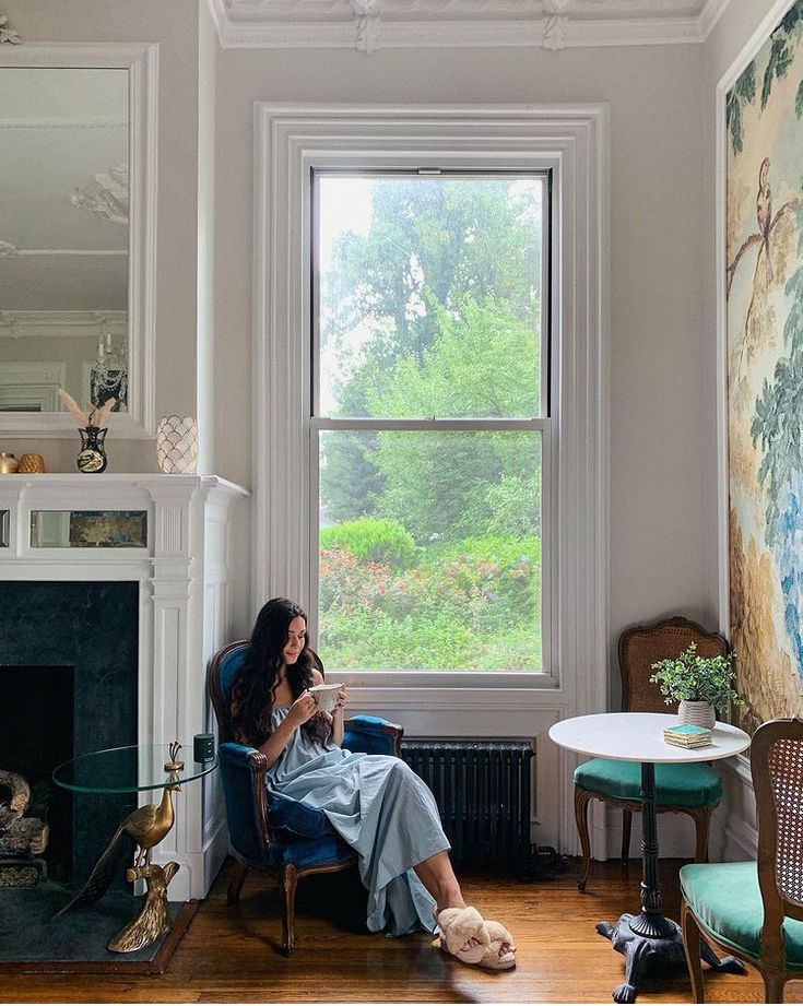 a woman sitting in a chair looking at her cell phone next to a fire place