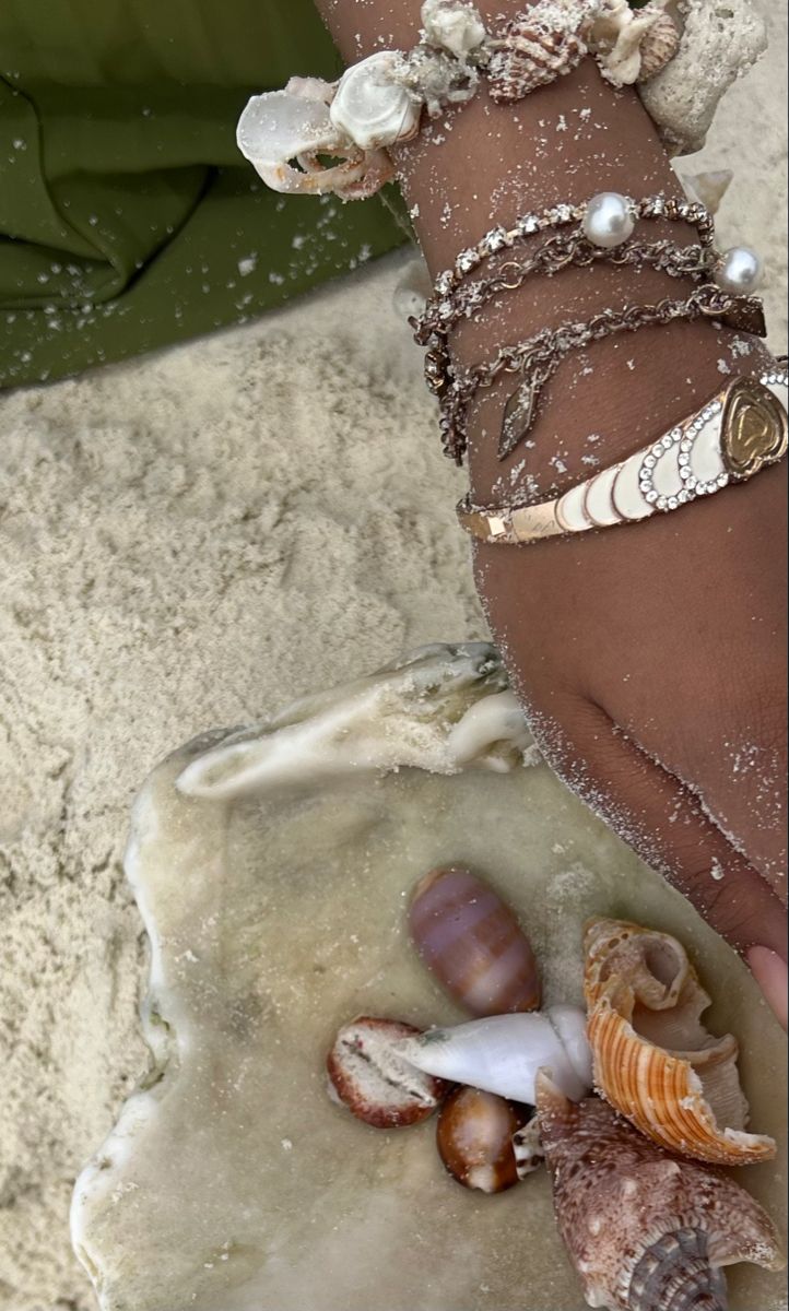 a woman's arm covered in shells and seashells, with her hand on the sand