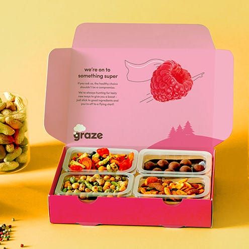 a pink box filled with lots of different types of food next to a jar full of nuts