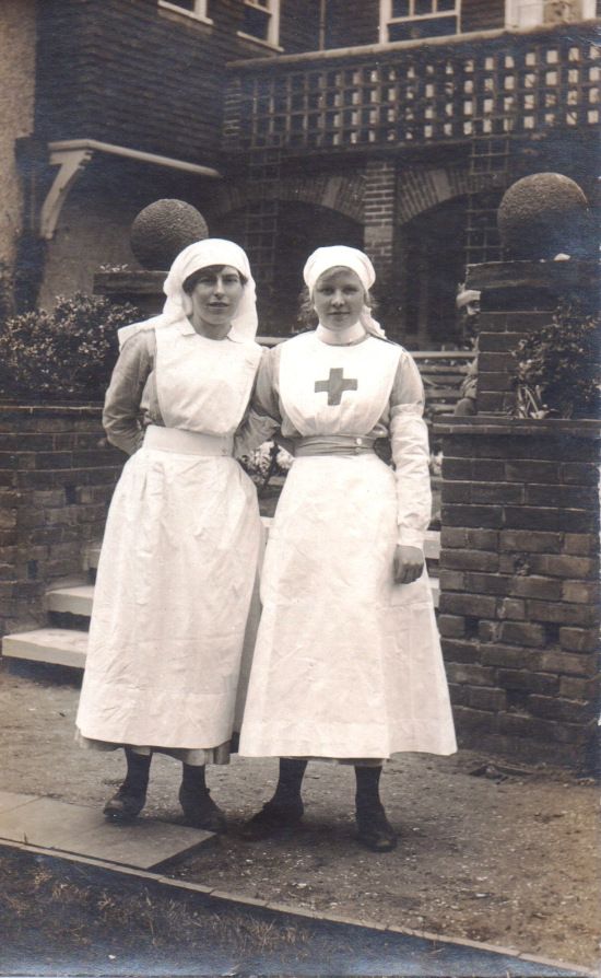 two women in white dresses standing next to each other on the sidewalk outside a house