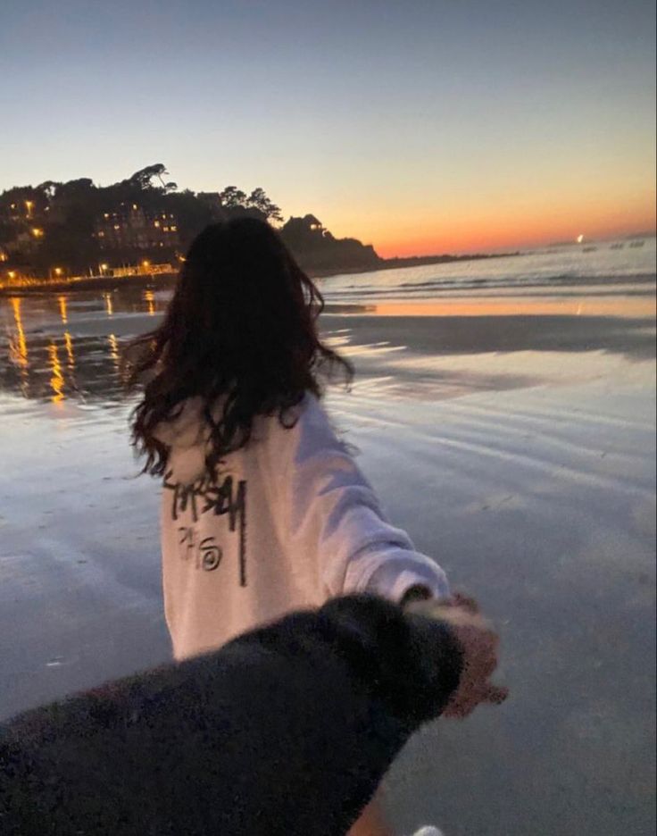 a woman walking on the beach with her dog at sunset or sunrise, holding hands