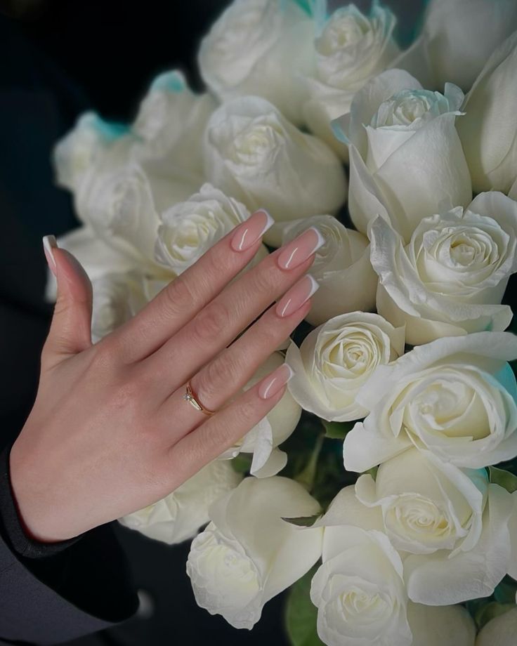 a woman's hand with pink manicures on her nails next to a bouquet of white roses