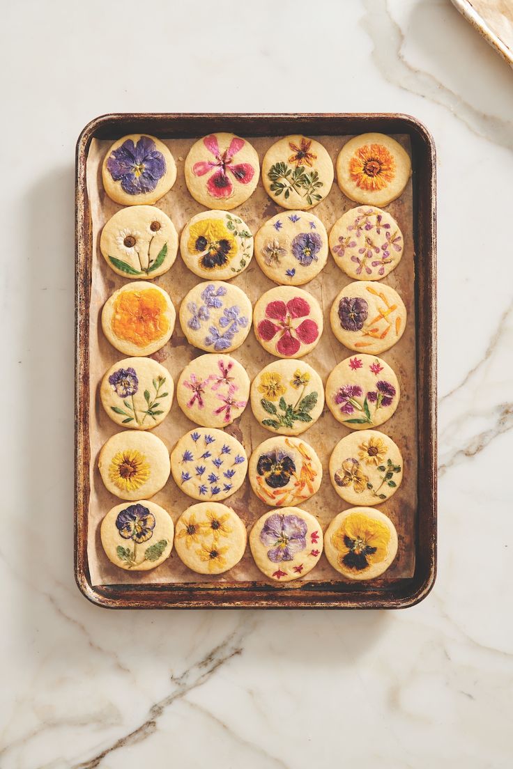 a baking pan filled with decorated cookies on top of a marble counter