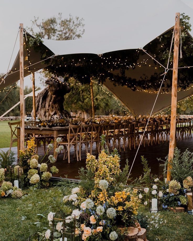 an outdoor tent set up with flowers and candles