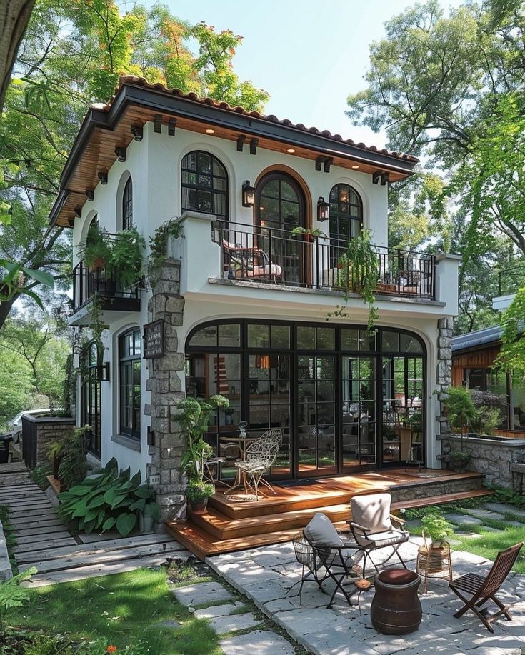 a large white house with lots of windows and plants on the front porch, surrounded by greenery