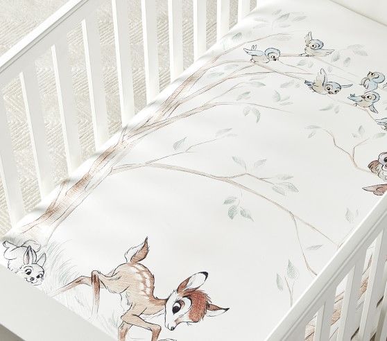 a baby crib with a cartoon deer on the sheet and other animals around it