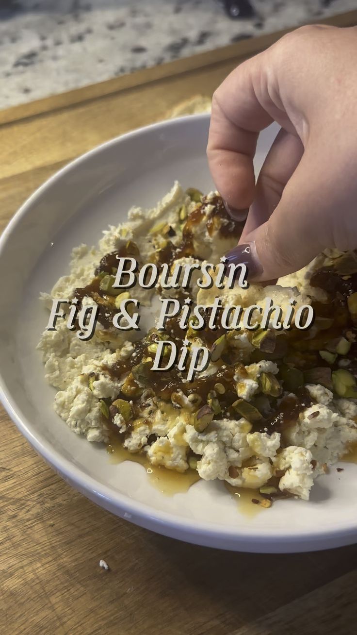 a person picking up food from a white plate on a wooden table with the words bourbon fig & pistachio dip