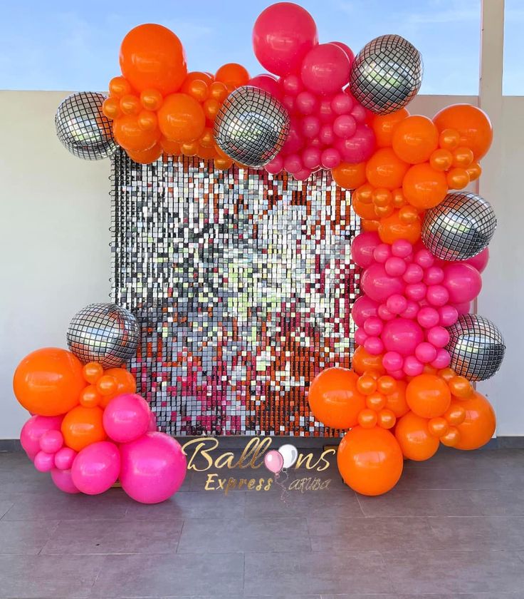 an orange, pink and silver balloon arch with disco balls in the middle on a tiled floor