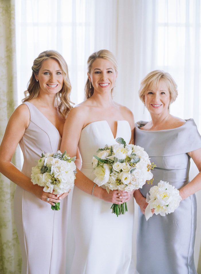 three bridesmaids pose for a photo in front of the window with their bouquets