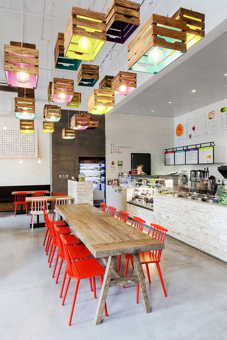 a restaurant with red chairs and wooden tables in front of a counter area that has colorful lights hanging from the ceiling