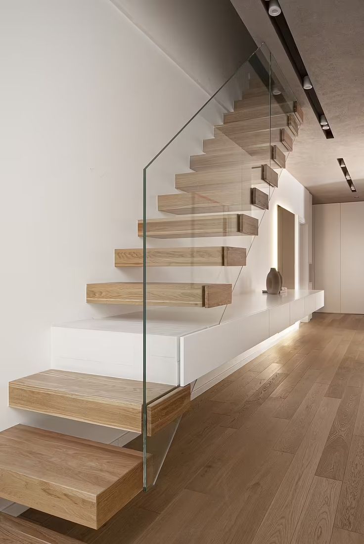 a wooden staircase with glass balconies in a white room next to hardwood floors