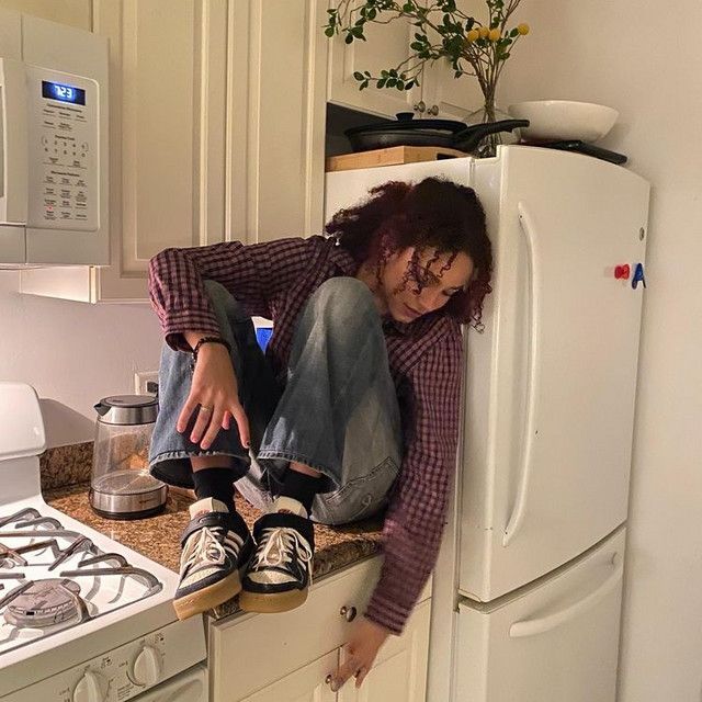 a woman sitting on top of a kitchen counter next to a white refrigerator freezer