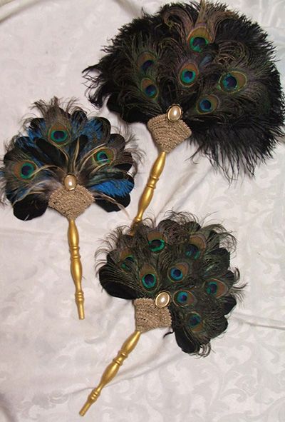 three peacock feathers with gold stems and pearls on the ends are sitting on a white sheet