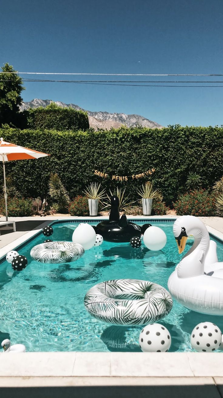 an inflatable swan float floating on top of a pool surrounded by balls and palm trees