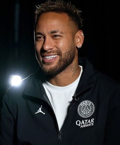 a smiling man in a black jacket and white t - shirt with his head turned to the side