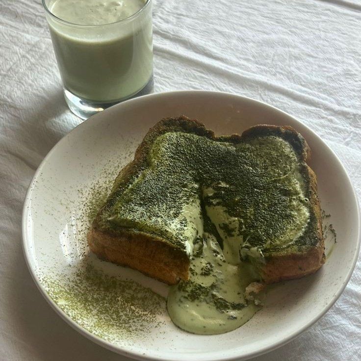 a white plate topped with two pieces of toast covered in pesto next to a glass of milk