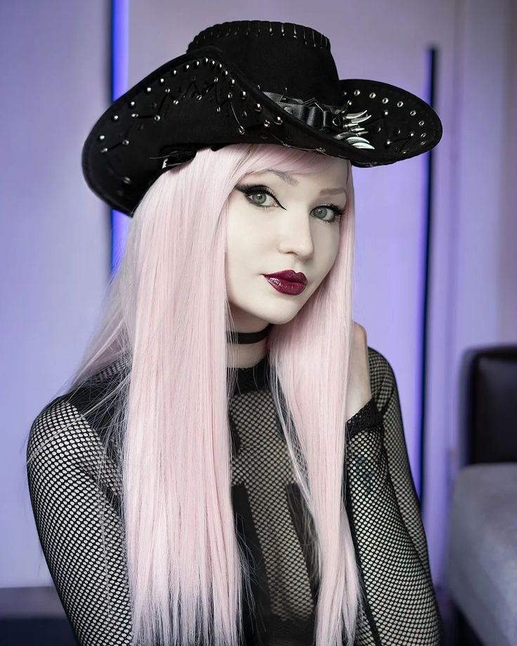 a woman with long pink hair wearing a black hat and mesh shirt, posing for the camera