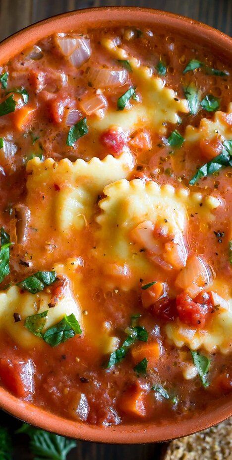 a bowl filled with pasta and sauce on top of a wooden table next to bread