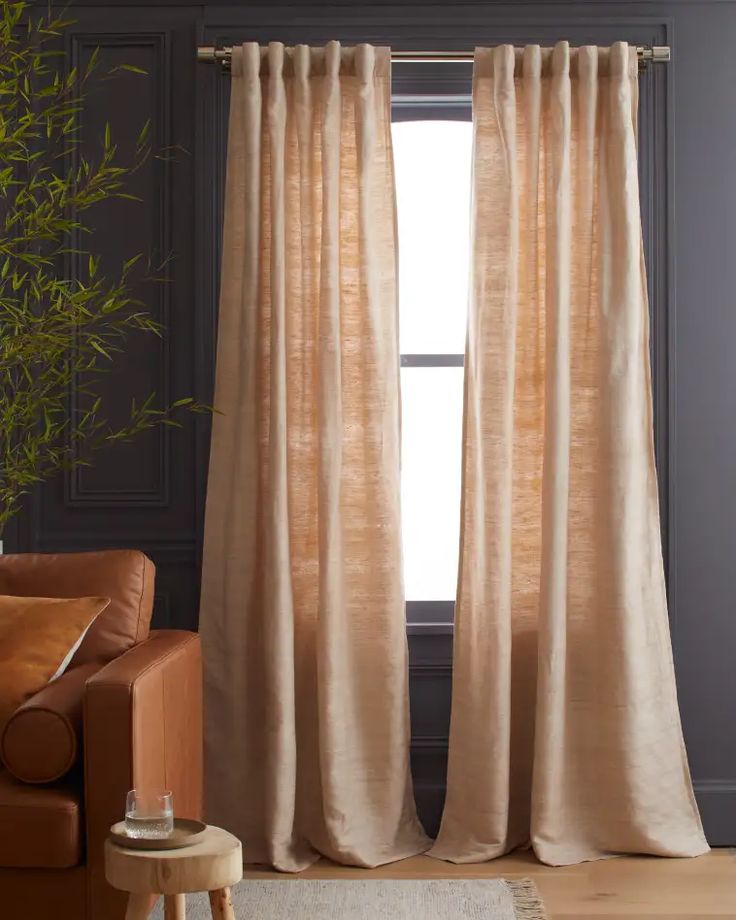 a living room with a couch, chair and window covered in beige drapes next to a potted plant