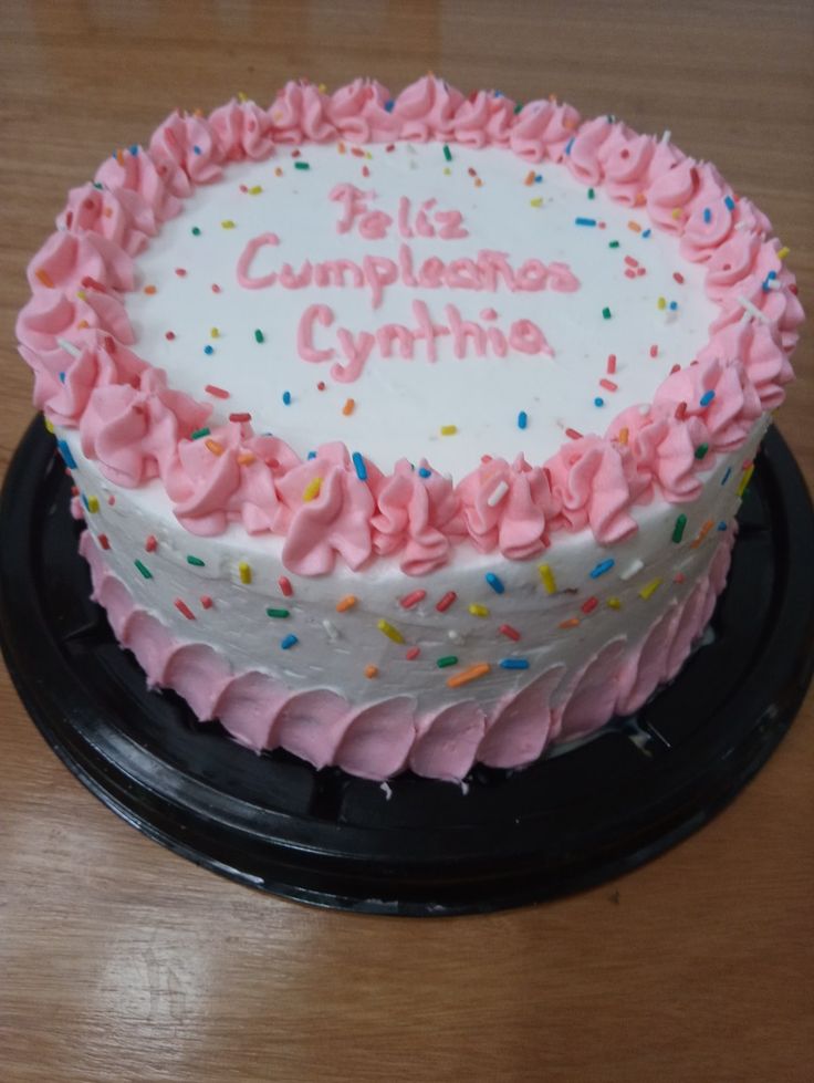 a birthday cake with pink frosting and sprinkles on the top is sitting on a black plate