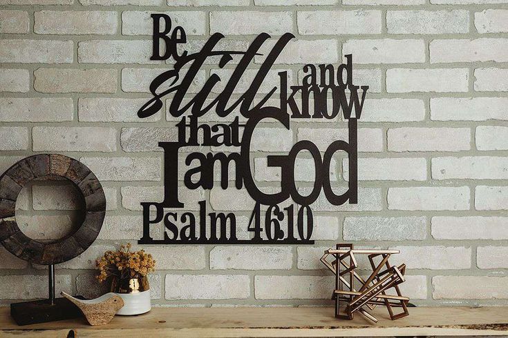 a wooden table sitting next to a brick wall with a metal sign that says be still and know that i am god