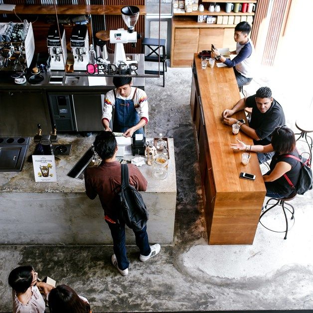 several people are sitting at the counter in a coffee shop and one person is using his cell phone