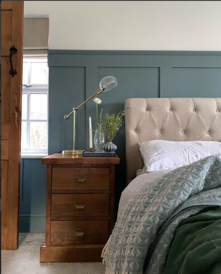 a bed sitting next to a wooden dresser with a lamp on it's side