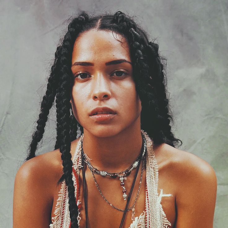 a woman with dreadlocks and necklaces on her chest looking at the camera