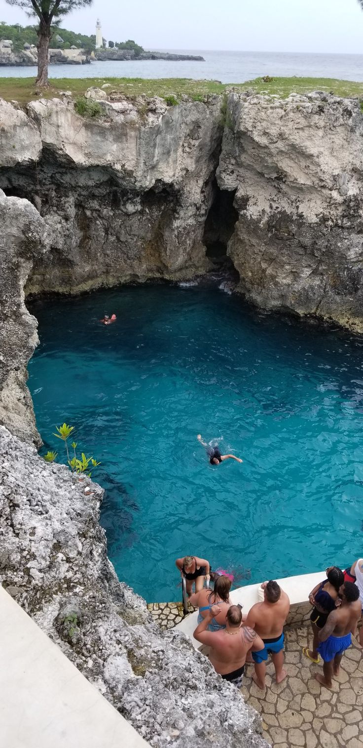 people are swimming in the blue water near some cliffs