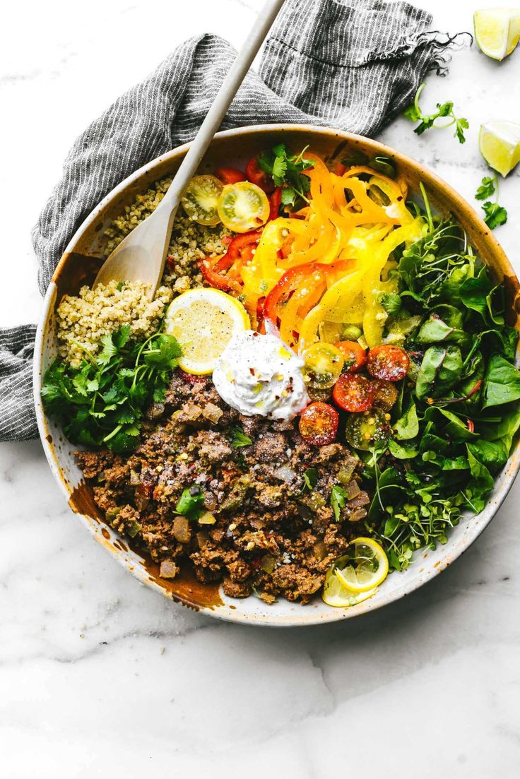 a bowl filled with meat and vegetables on top of a marble countertop next to a wooden spoon