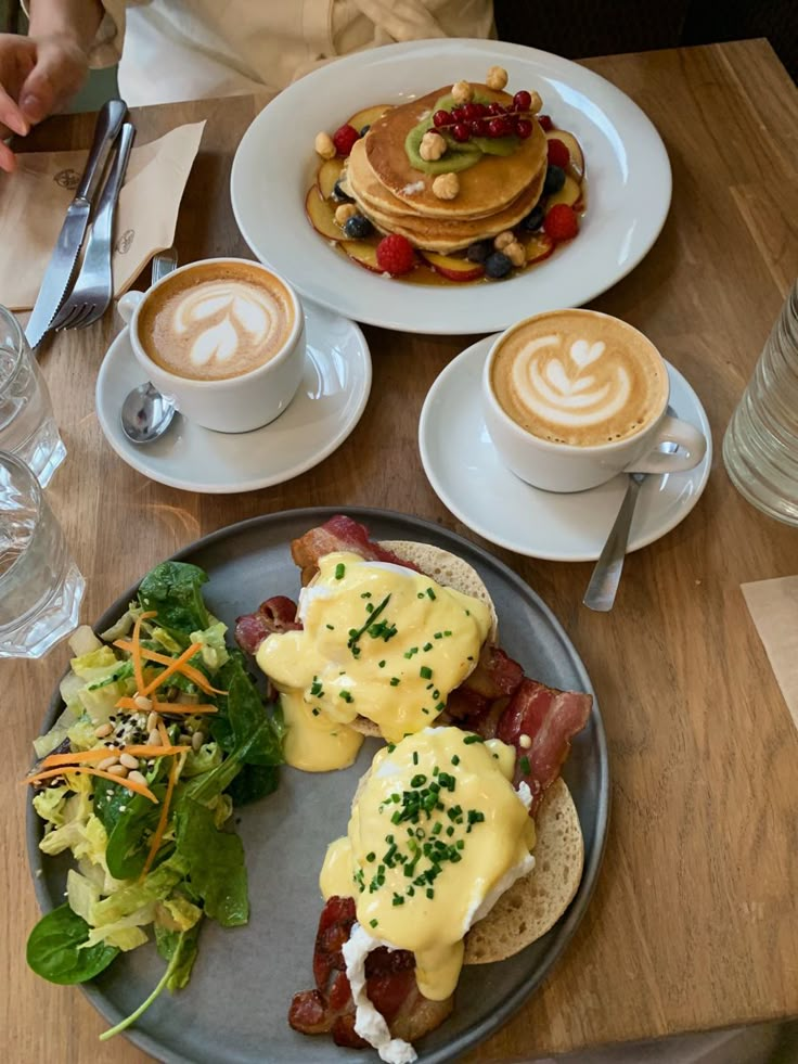 breakfast plates with eggs, bacon, pancakes and salad on a table at a cafe