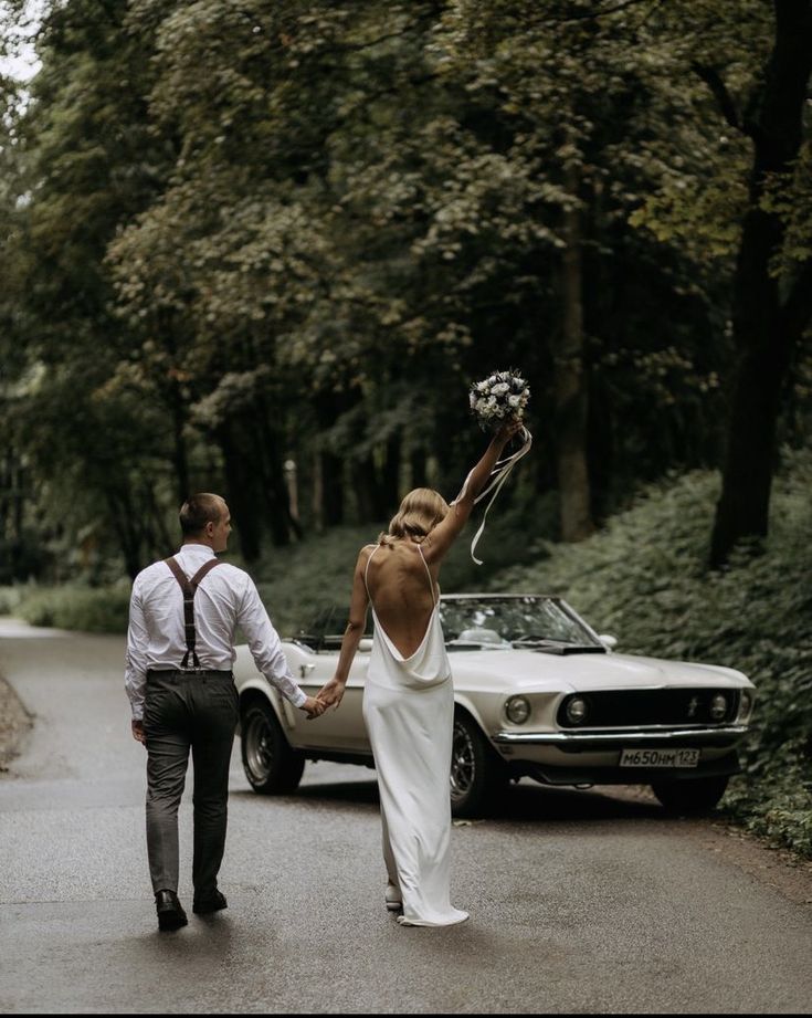 a bride and groom walking down the road holding hands with an old car in the background