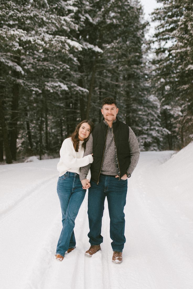 a man and woman are standing in the snow near some trees with their arms around each other