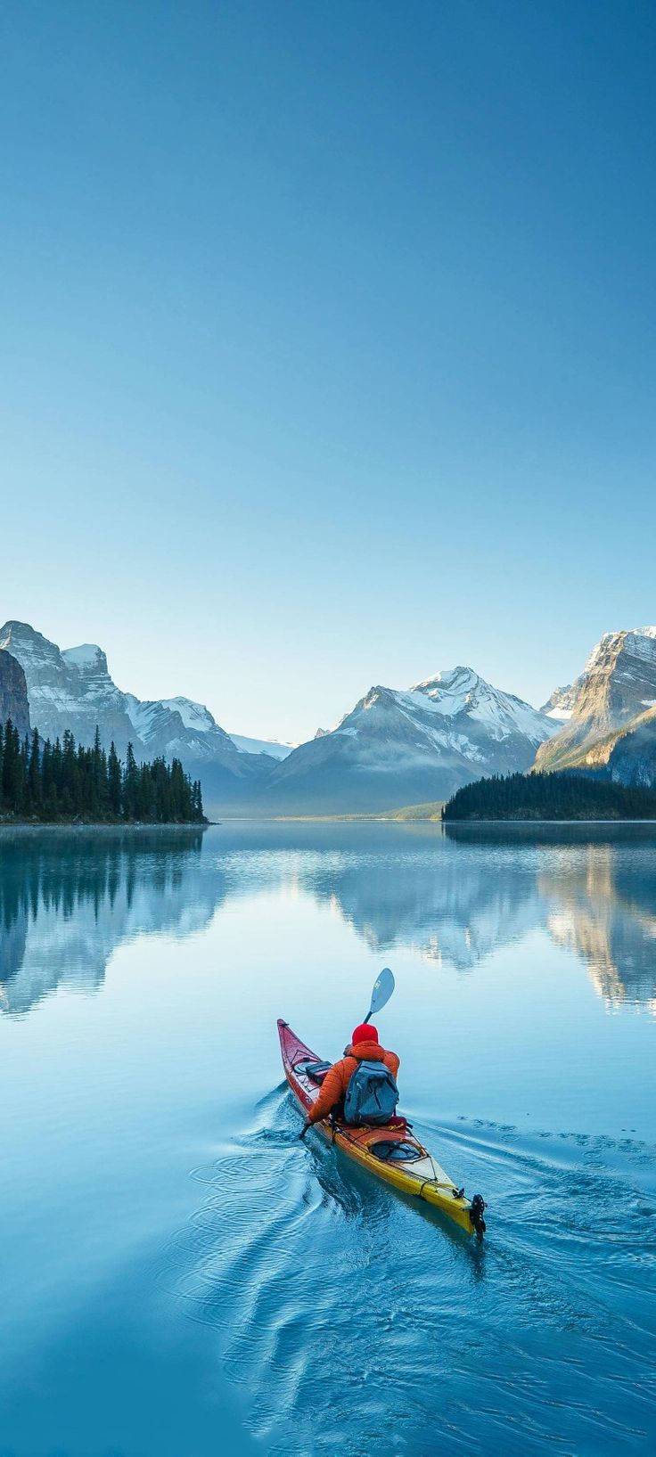 a person in a kayak paddling on the water with mountains in the background