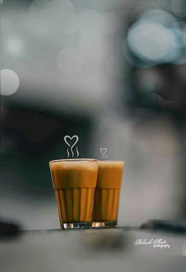 two glasses filled with liquid sitting next to each other on top of a table in front of a blurry background