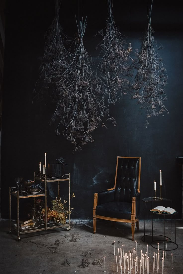 a chair and table with candles hanging from the ceiling in front of a black wall